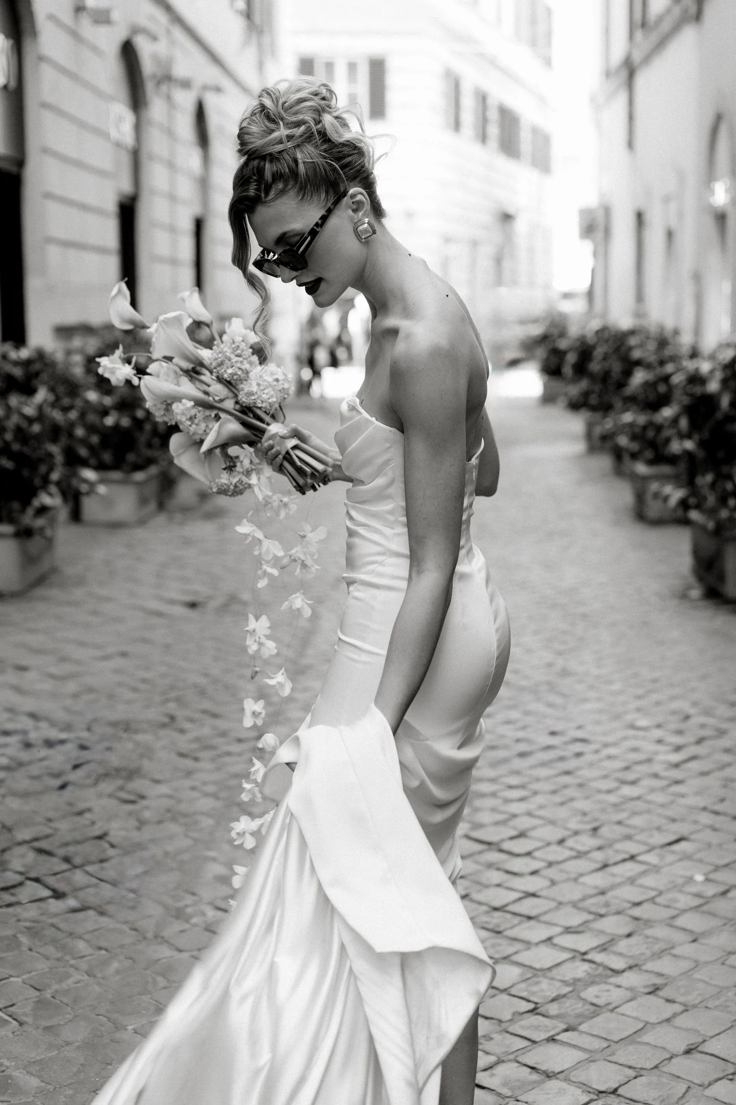 Black and white portrait of a bride carrying her bouquet through a Roman street