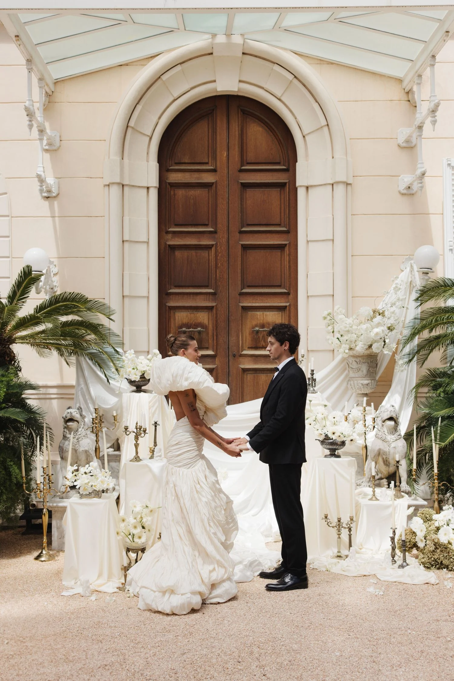 Couple before carved wooden doors flanked by white floral pedestals