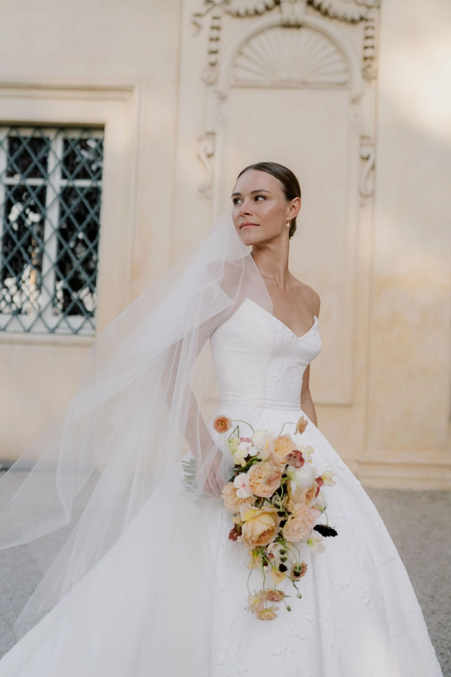 Bride with a peach garden rose bouquet against a warm villa wall