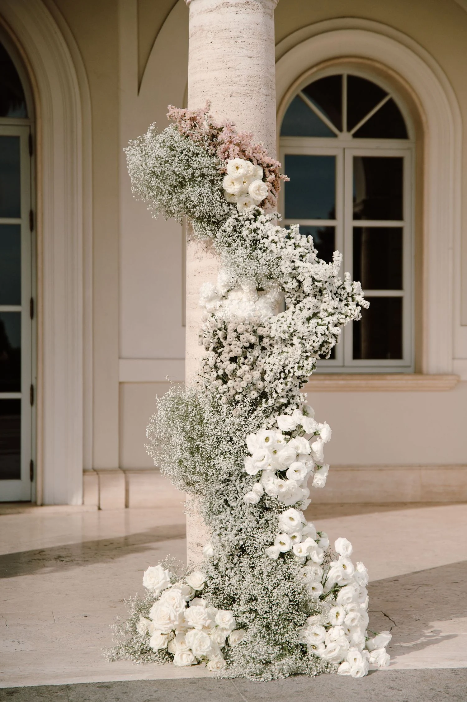 Spiralling white floral column of roses and gypsophila against a villa facade
